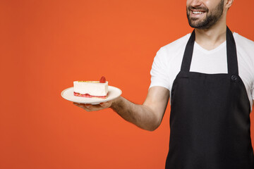 Close up cropped shot man barista bartender barman employee in black apron white t-shirt work coffee shop giving sweet cake dessert isolated on orange background studio Small business startup concept.