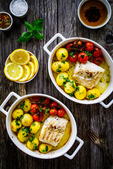Fish dish - baked cod fillet with potatoes and cherry tomatoes on wooden table
