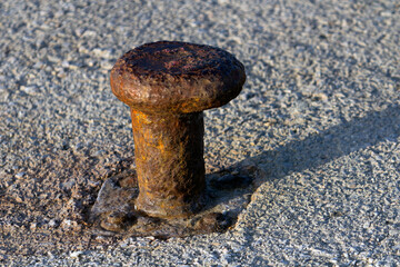 High angle view of a rusted bollard with worn out screws on rough, large grained cement ground under evening sun.Concept image for travel, trust, transportation, reference point.