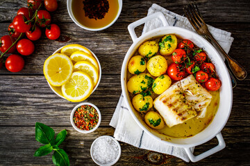 Fish dish - baked cod fillet with potatoes and cherry tomatoes on wooden table
