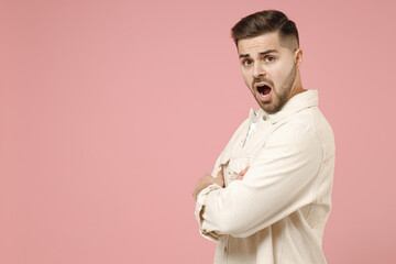 Young side profile view indignant confused caucasian man 20s in jacket white t-shirt holding hands crossed folded isolated on pastel pink color background studio portrait. People lifestyle concept