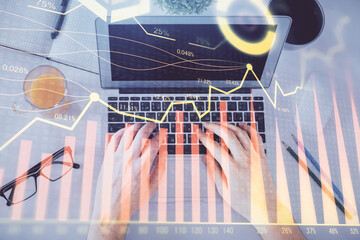 Double exposure of man's hands typing over laptop keyboard and forex chart hologram drawing. Top...