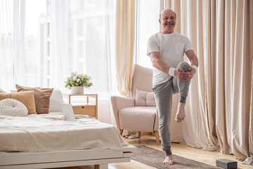 Elderly man practicing yoga or fitness standing on tree pose at home.