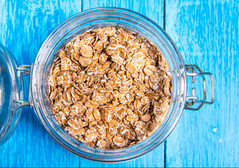 Close-up of opened jar of whole oat flakes, heap of oatmeals to prepare porridge on vintage blue wooden desks background. Top view. Copyspace.