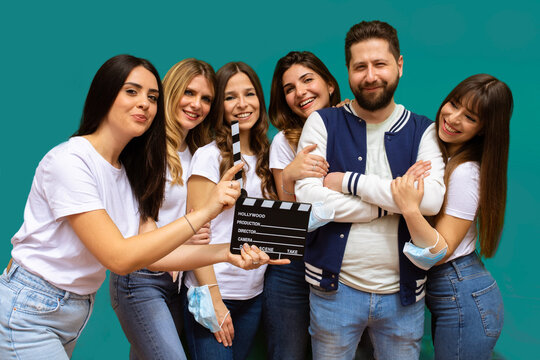 group of smiling young friends taking a selfie while holding a movie clapperboard in hand isolated on light blue background