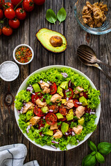 Tuna salad - tuna, cherry tomatoes, avocado, lettuce and onion on wooden table
