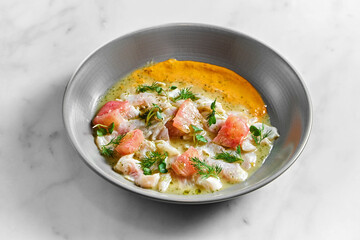 Peruvian cuisine dish - seabass ceviche with grapefruit and yellow sauce, served in a grey plate on a marble background. Restaurant seafood.