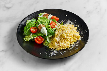 Scrambled omelet with spinach salad, ricotta cheese and cherry tomatoes, served in a black plate on a marble background. Delicious breakfast