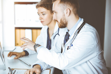 Red-bearded doctor with female colleague discussing current disease therapy while sitting at...