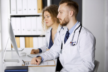 Male doctor withcolleague discussing current disease therapy while sitting at working place in...