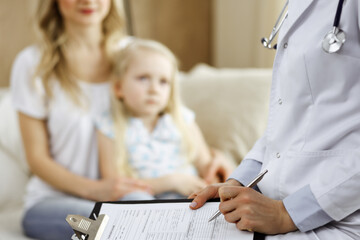 Doctor and patient. Pediatrician using clipboard while examining little girl with her mother at home. Sick and unhappy child at medical exam. Medicine concept