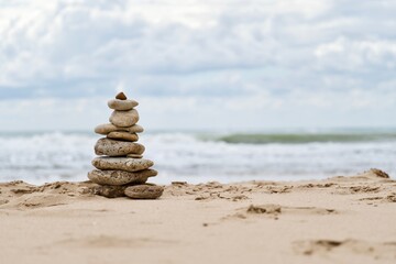 Fototapeta na wymiar Stones stacked (trail cairn) on empty beach on a sunny day with a cloudy sky and the ocean in the back
