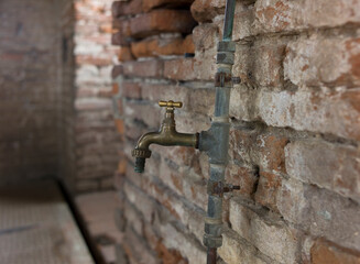 Room in a ruin with a dilapidated old brick wall and a copper water tap or faucet that is somewhat loosely attached to the wall