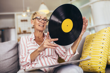 Happy senior woman listening vinyl at home. Choosing next record.
