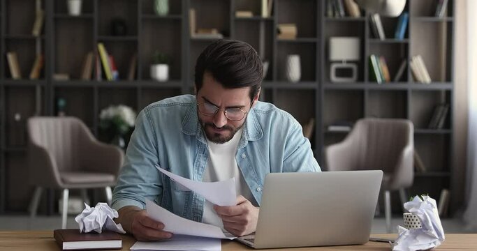 Anxious stressed young male manager employee entrepreneur in eyeglasses crumping paper documents, feeling nervous analyzing data statistics reports, standing and leaving workplace, deadline concept.