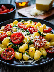 Gnocchi with tomato, spinach and parmesan  on wooden table
