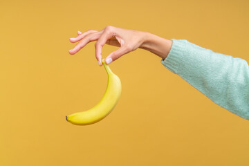 Female hand holding a banana with two fingers tips