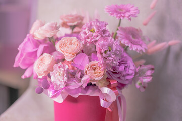 A lush bouquet of pink, purple, peach colour, white cute delicate small roses of different sizes, flowers in cylindrical bright box vase on a table in the studio