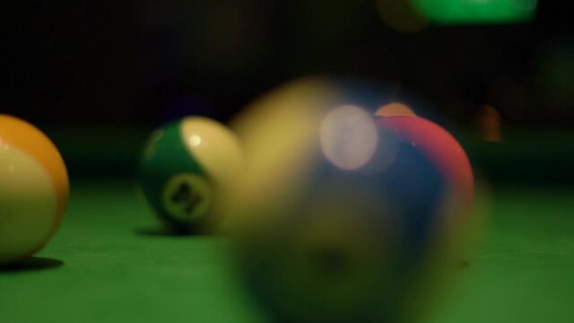 Motion past billiard balls with numbers lying on modern pool table covered with green velvet fabric in semi-dark bar hall extreme closeup.