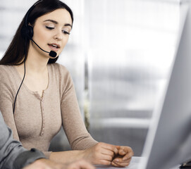 Two young people in headsets are talking to the clients, while sitting at the desk in an office....