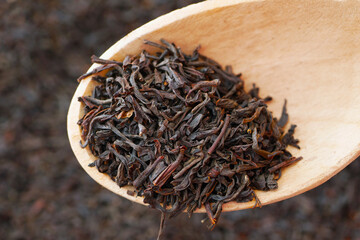 black loose long leaf tea in wooden spoon