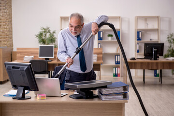 Fototapeta na wymiar Old businessman employee holding vacuum cleaner at workplace