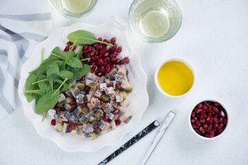 Herring tartar with pomegranate and fresh spinach on a shell-shaped plate, top view on a white stone background