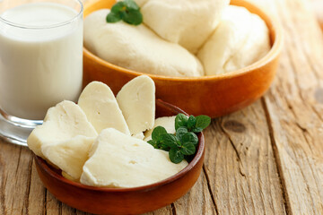 Cypriot semi-hard, fresh homemade unripened brined cheese halloumi in wooden plates and milk. popular in the Levant, Greece and Turkey.Side view in wicker busket on rustic wooden background,close up