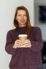 Soft focus pretty young woman in stylish violet sweater holding cup in hands. Warm soft cozy image. Details. Drinking take away coffee. Breakfast on the go. Instagram style toned image. Focus on cup