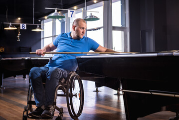 Adult man with disability in a wheelchair play billiards in the club