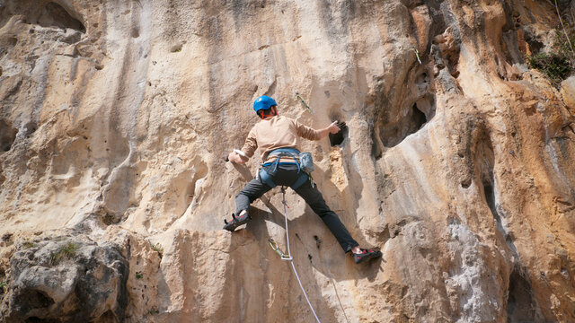Joven barbudo escalador con casco azul rapelando con cuerda una pared rocosa