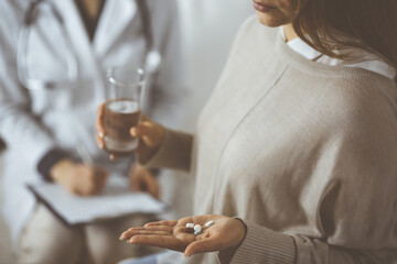 Close-up woman-patient holding pills near her doctor, time to take medications, cure for headache or remedy pain killer drugs. Stay at home concept during Coronavirus pandemic and self isolation