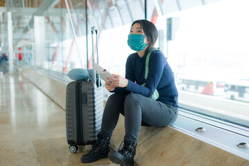 Fototapeta premium Asian woman flying in covid19 times - young tired and attractive Korean girl in face mask waiting on airport with her flight suffering delay feeling unhappy