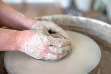 Woman working on potter's wheel. Hands sculpt cup from white clay pot. Workshop on modeling do plate. Potter works on potter's wheel. Concept:handmade, workshop, artist. 