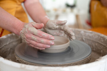 Woman working on potter's wheel, makes cup. Hands sculpt cup from white clay pot. Workshop on modeling do plate.  Concept: handmade, workshop, artist. Close-up.