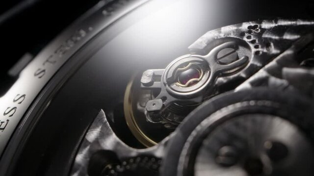 Swiss watch back cover with full open mechanism and balance rotating on black background. Gears, stainless steel lettering and jewels extreme closeup 