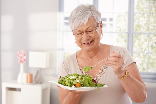 Happy old lady eating fresh green salad, smiling.