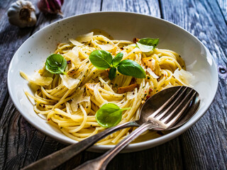 Spaghetti aglio e olio with parmesan and basil on wooden table
