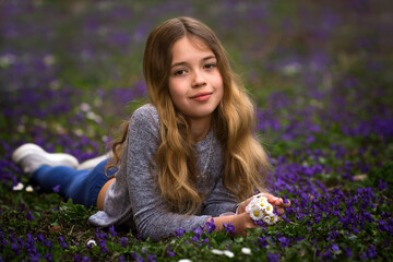 Young girl lying on lawn with violet flowers in park. Kid portrait and spring blossom.