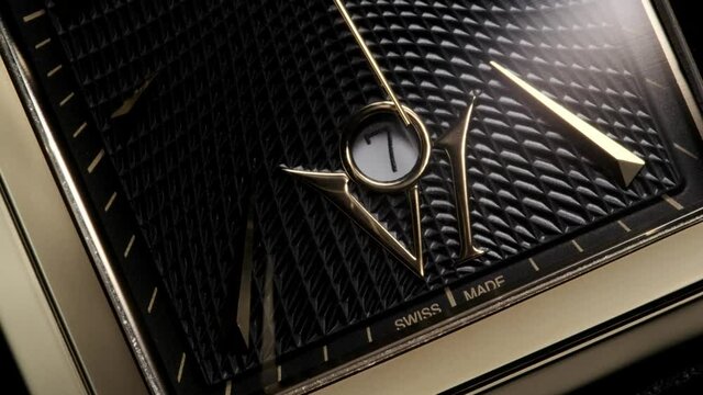Luxury golden swiss made watch with square body and waffle pattern on clockface rotating while second arrow is passing by the date and numbers. Closeup with zoom-out effect