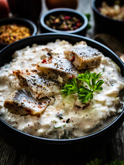 Marinated herring fillets in cream with pickled cucumber, parsley, onion and apple on wooden table 