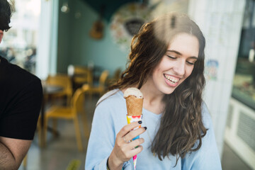 Chica joven tomando helado en cafeteria vista a través de un cristal