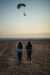 DOS CHICAS PASEANDO DE ESPALDAS POR LA ARENA DE LA PLAYA AL ATARDECER