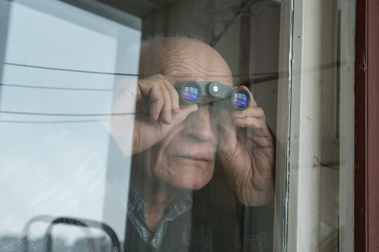 Aduld bald man looking through window glass with binoculars