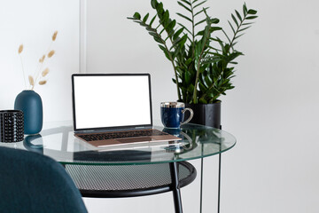 Laptop wiith white screen on wooden table in home scandi interior. Stylish minimalistick workplace, copy space