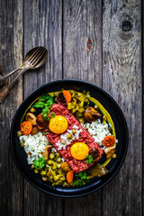 Perfect beef tartare steak with onion, capers, pickled cucumbers and mushrooms on wooden table
