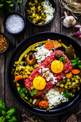 Perfect beef tartare steak with onion, capers, pickled cucumbers and mushrooms on wooden table
