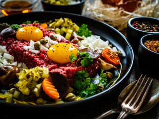 Perfect beef tartare steak with onion, capers, pickled cucumbers and mushrooms on wooden table
