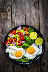 Sunny side up eggs with avocado, cherry tomatoes, toasted bread and red onion on wooden table

