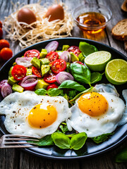 Sunny side up eggs with avocado, cherry tomatoes, toasted bread and red onion on wooden table

